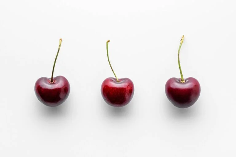 three cherries on a row on a white surface