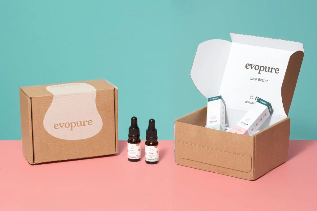 Two Evopure CBD oil bottles beside a kraft Evopure gift box and an open mailer box with product cartons