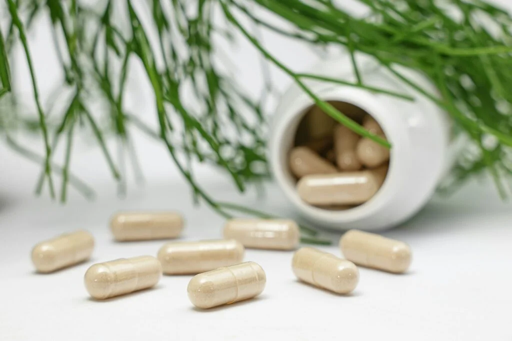 Supplement capsules in front of an open bottle with green leaves