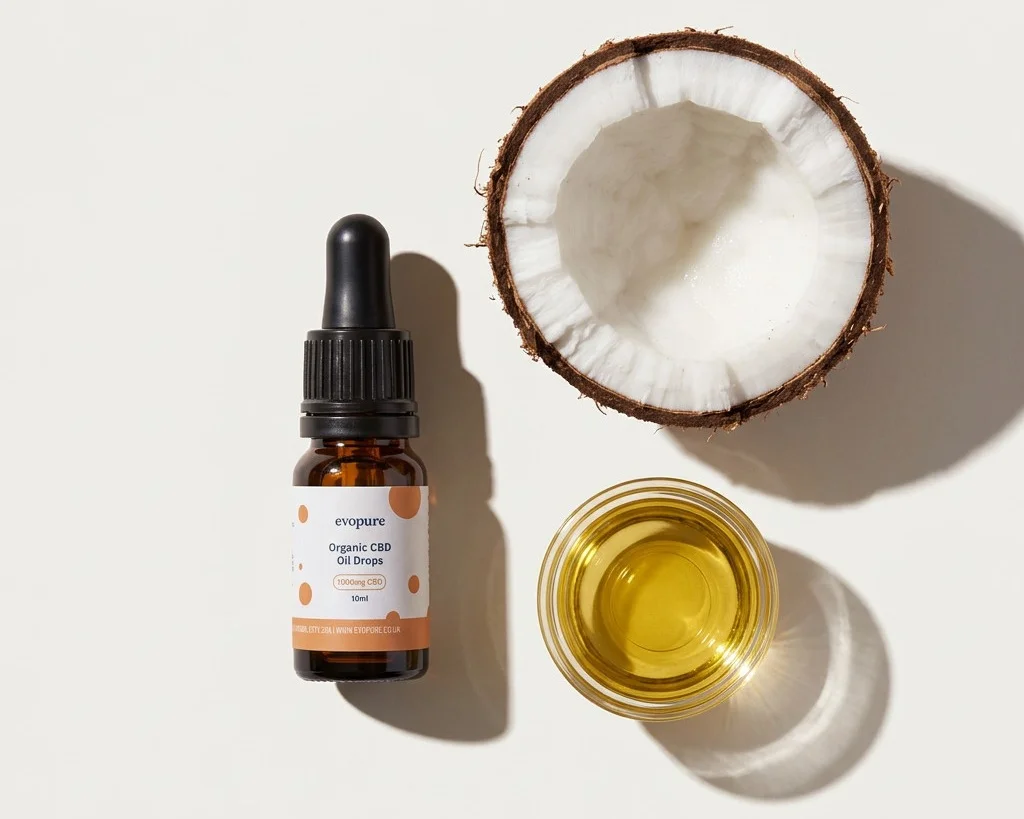 A bottle of Evopure broad spectrum CBD oil drops beside half a coconut and a small dish of MCT oil