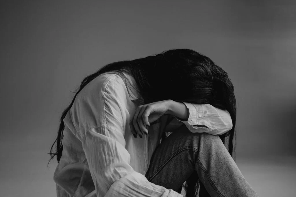 A tired woman sitting with her head resting on her knees, in black and white
