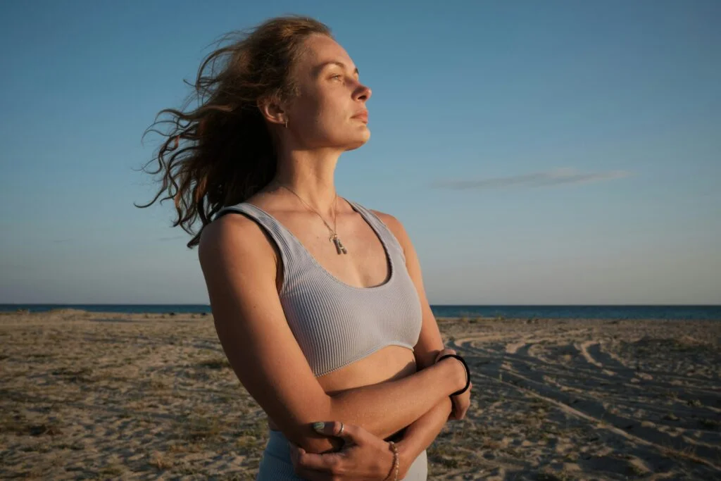 A woman standing on a beach at sunset with her eyes half closed, breathing calmly