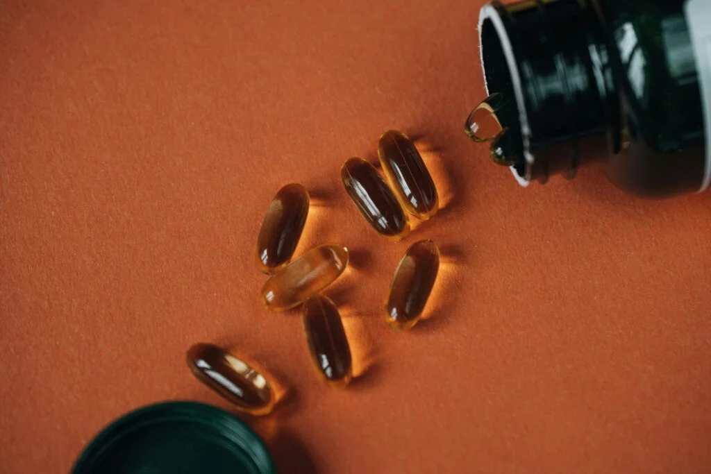 Amber softgel capsules spilling from a dark bottle onto an orange surface