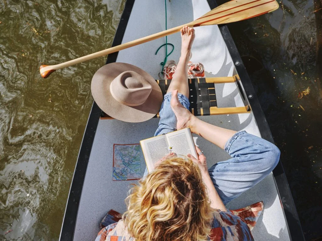 A woman reading a book in a canoe on the water, with no phone in sight