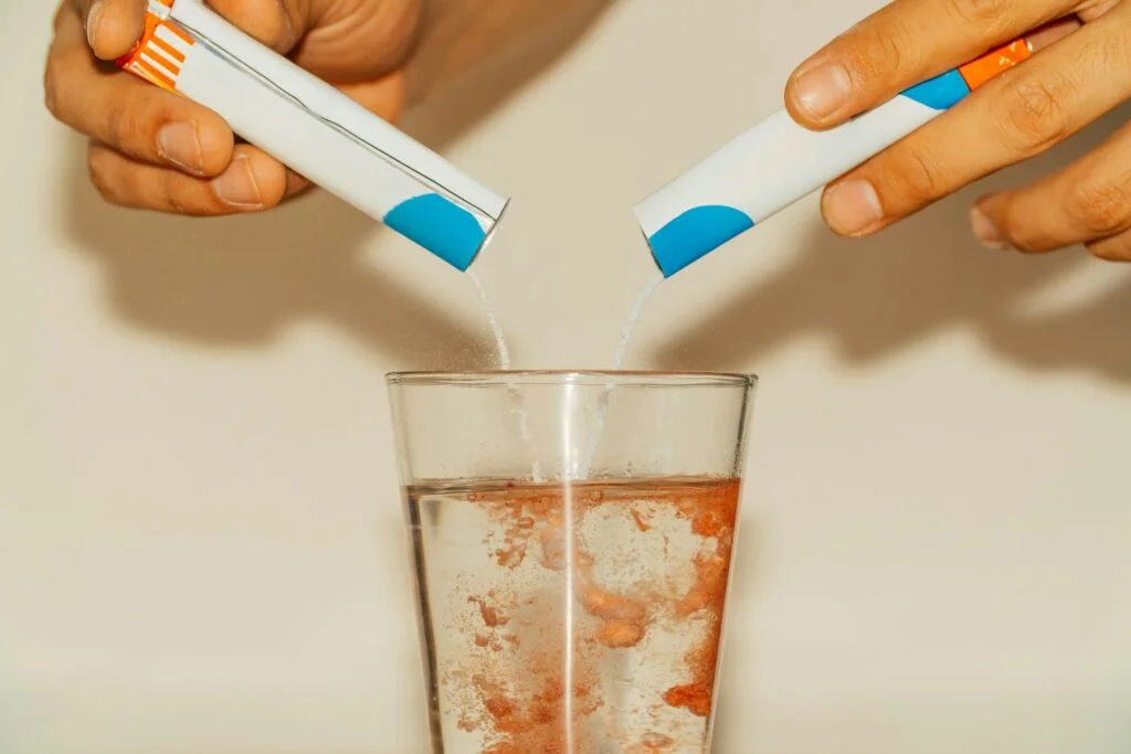 Two sachets of electrolyte powder being poured into a glass of water