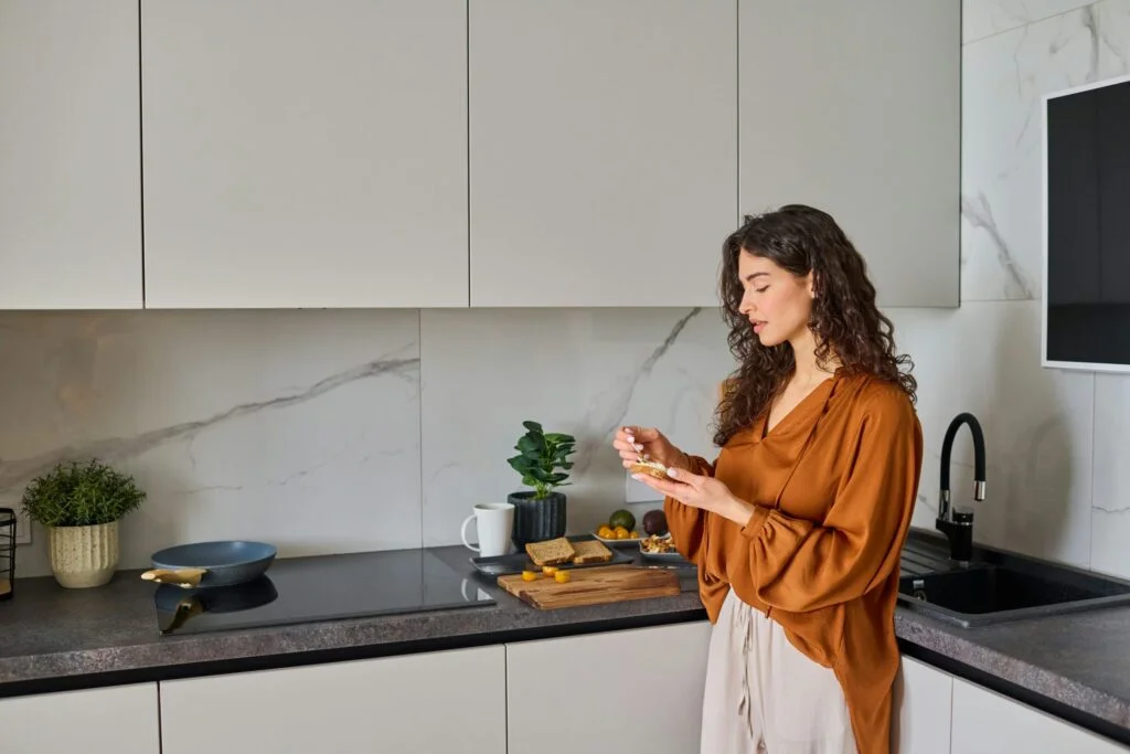 A woman in a bright kitchen taking a supplement at breakfast
