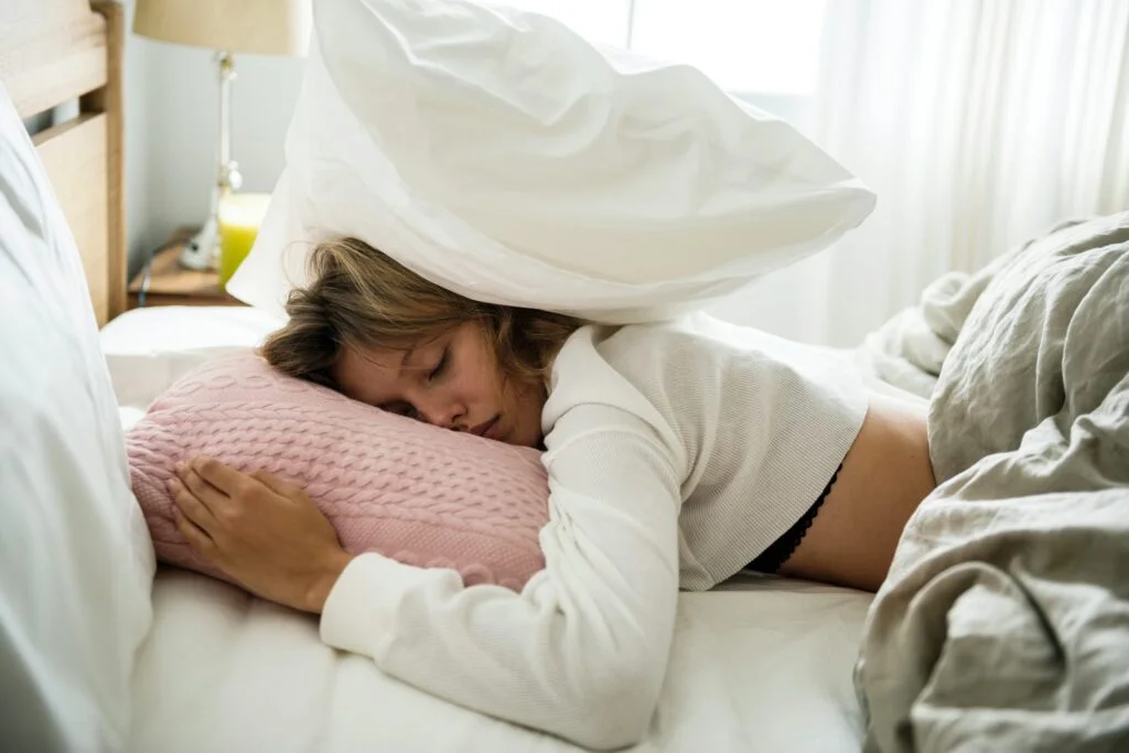 A woman asleep in bed with a pillow pulled over her head