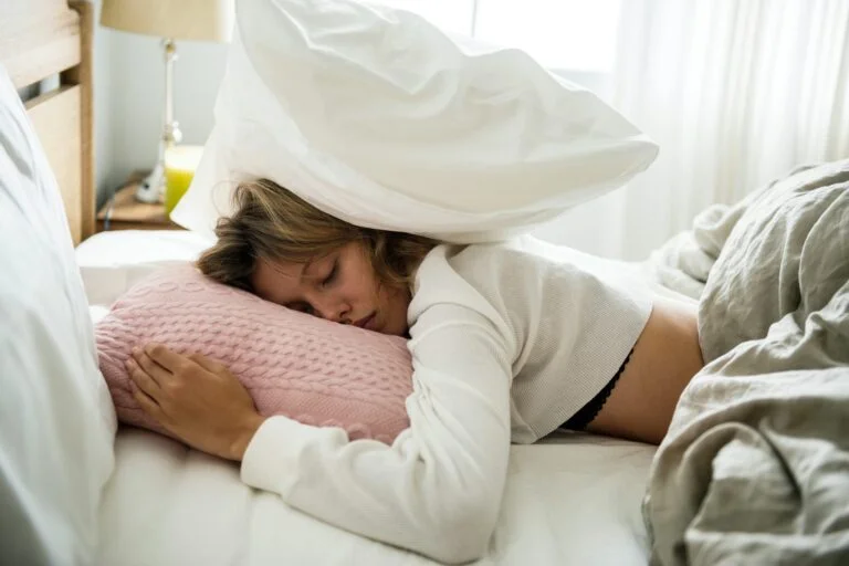 A woman asleep in bed with a pillow pulled over her head