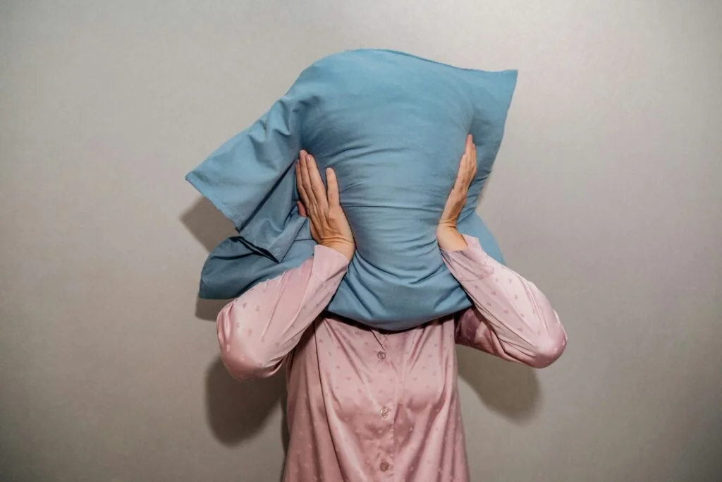 A person in bed holding a pillow over her head