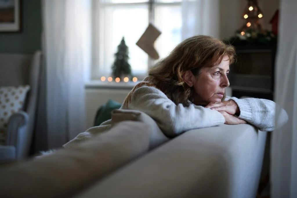 A thoughtful woman leaning on the back of a sofa, looking out of the window