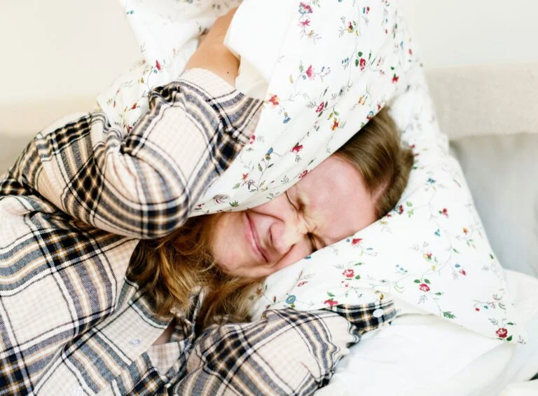 A frustrated person in bed pulling a pillow over their head, unable to sleep