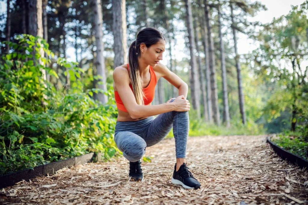 A woman crouching on a woodland path holding her sore knee