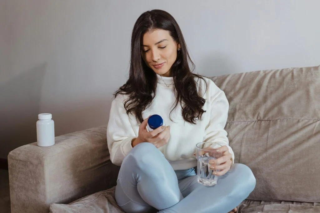 A woman on a sofa reading a supplement label with a glass of water