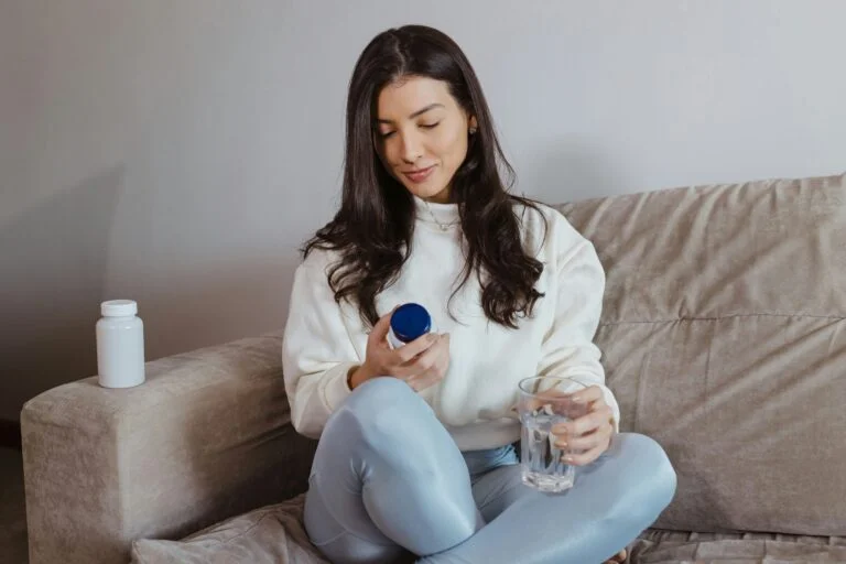 A woman on a sofa reading a supplement label with a glass of water