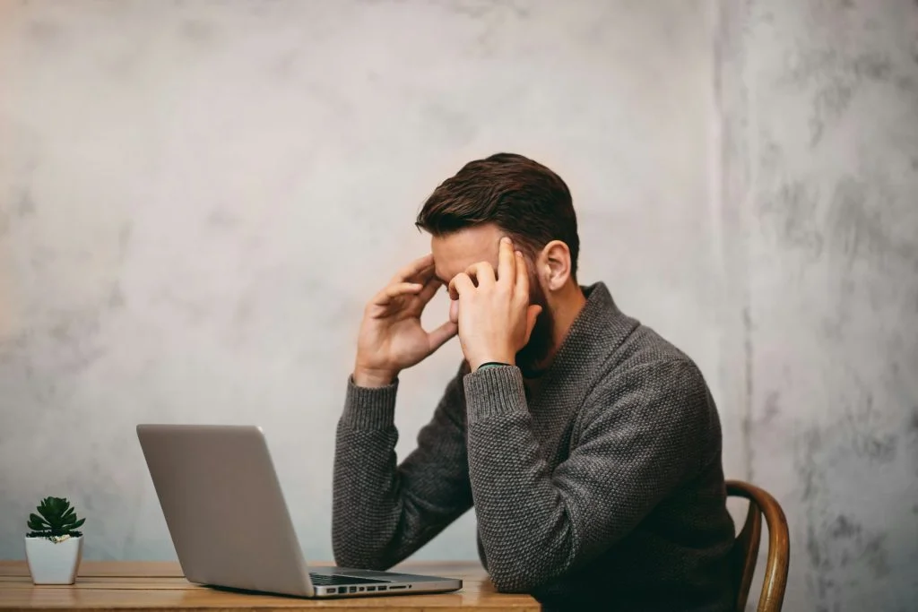 Man looking stressed whilst sitting down. Laptop in front of him
