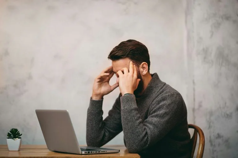 Man looking stressed whilst sitting down. Laptop in front of him