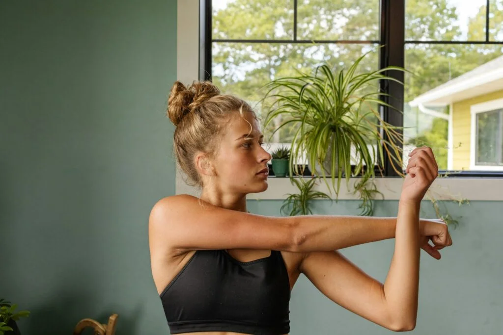 A woman doing an arm stretch by a window after a workout