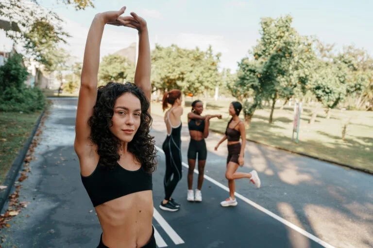A woman stretching outdoors in the sunshine with friends warming up behind her