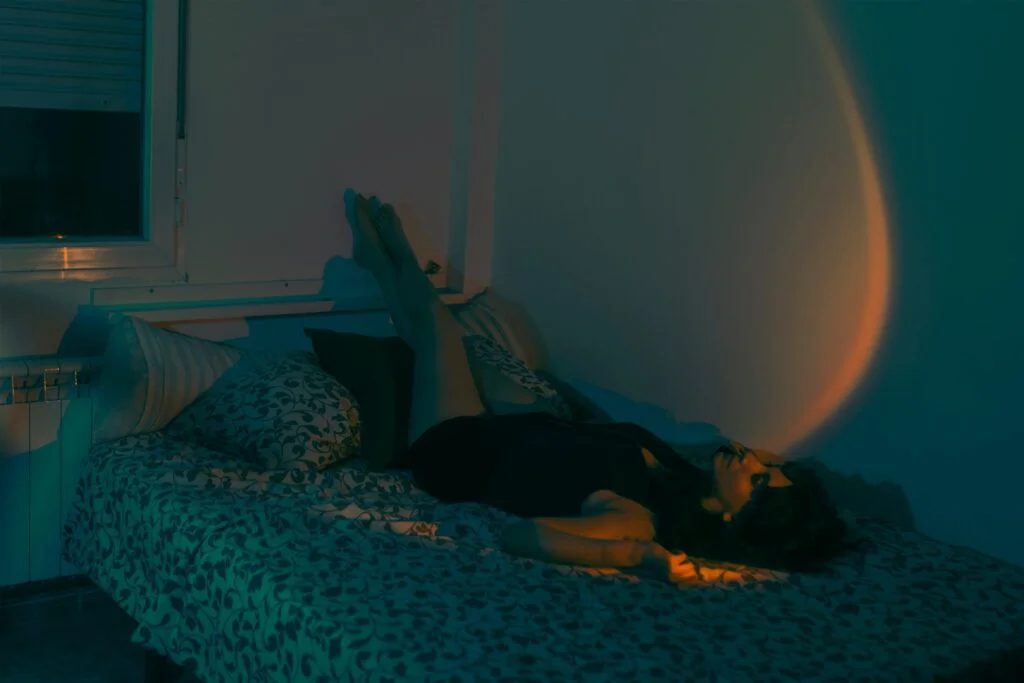 A woman lying restless on her bed at night with her legs up against the wall
