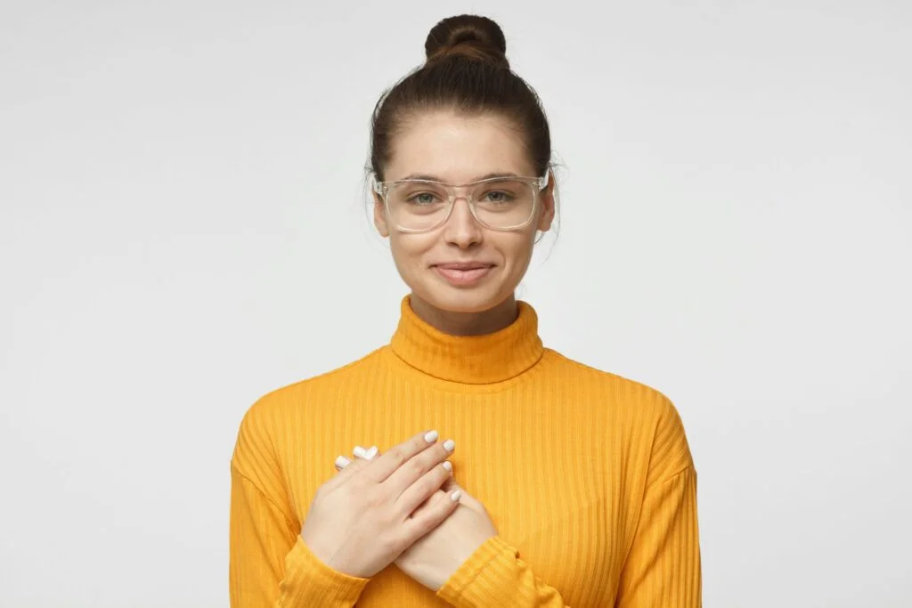A calm young woman in a yellow jumper with her hands crossed over her chest