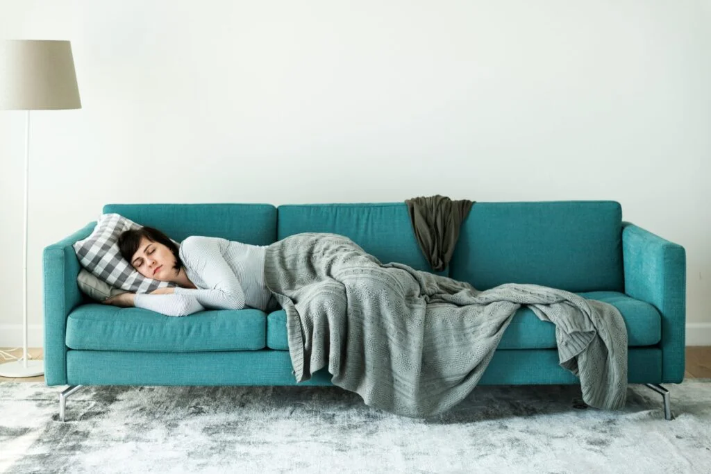 A woman taking a nap on a sofa under a grey knitted blanket