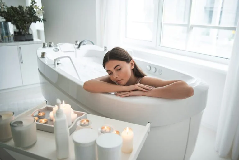 A woman relaxing with her eyes closed in a bath surrounded by lit candles