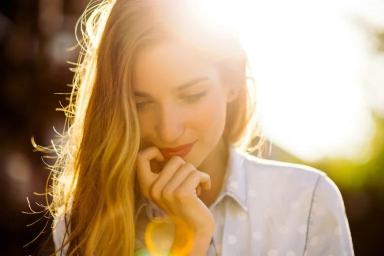 A smiling woman with long hair outdoors in warm golden sunlight