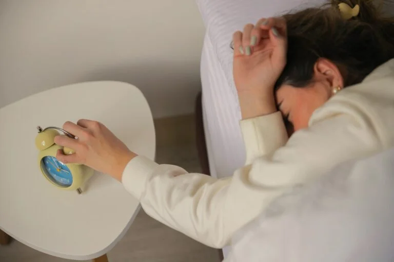 A sleepy woman in bed reaching out to switch off an alarm clock on her bedside table