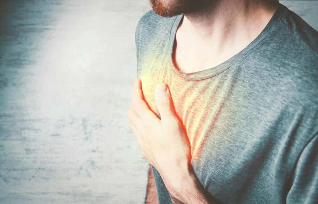 A man holding his hand to his chest, with a glow showing where heartburn is felt