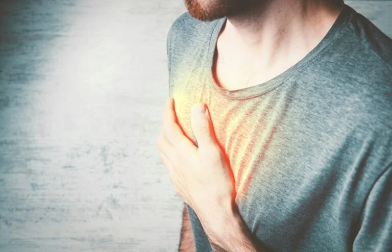A man holding his hand to his chest, with a glow showing where heartburn is felt