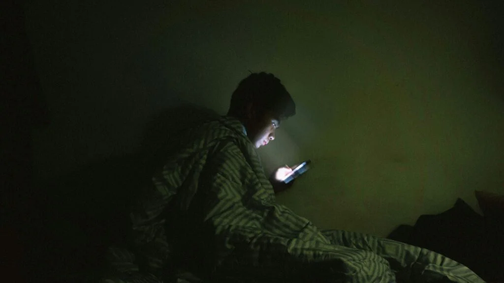 Person sitting up in bed at night looking at a phone