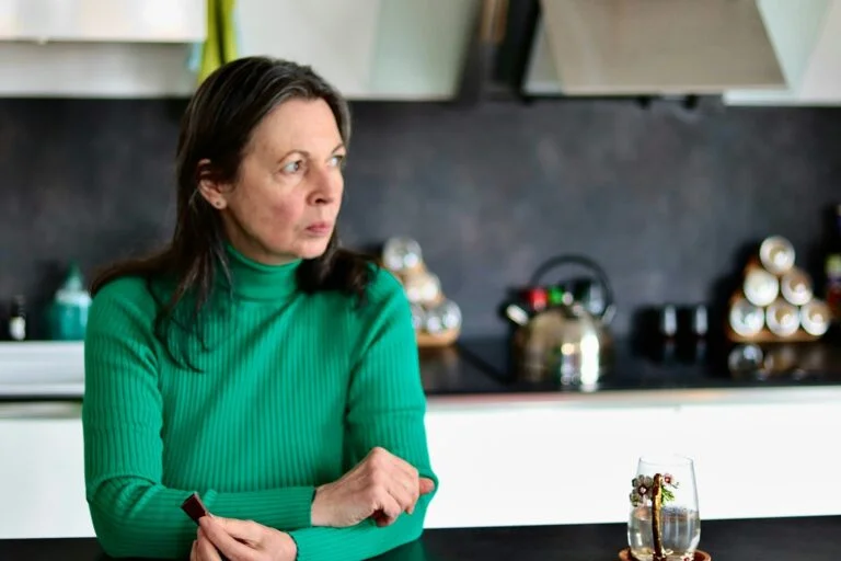 A woman sitting at her kitchen table looking into the distance with a worried expression