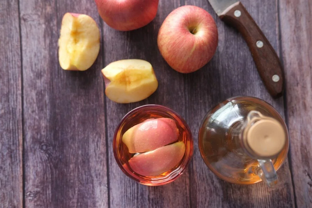 Sliced apples beside a glass of apple cider vinegar and a small glass jug