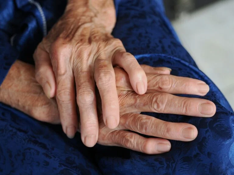Close-up of an older person's hands resting on blue fabric