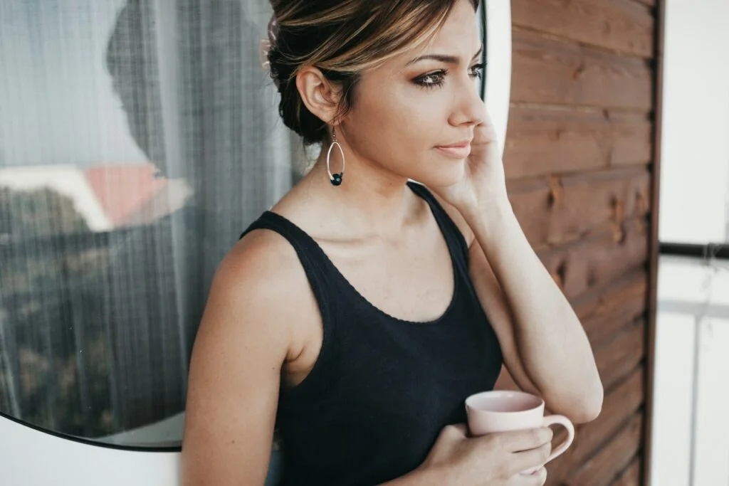 A woman holding a mug and looking out of a window, calm and thoughtful