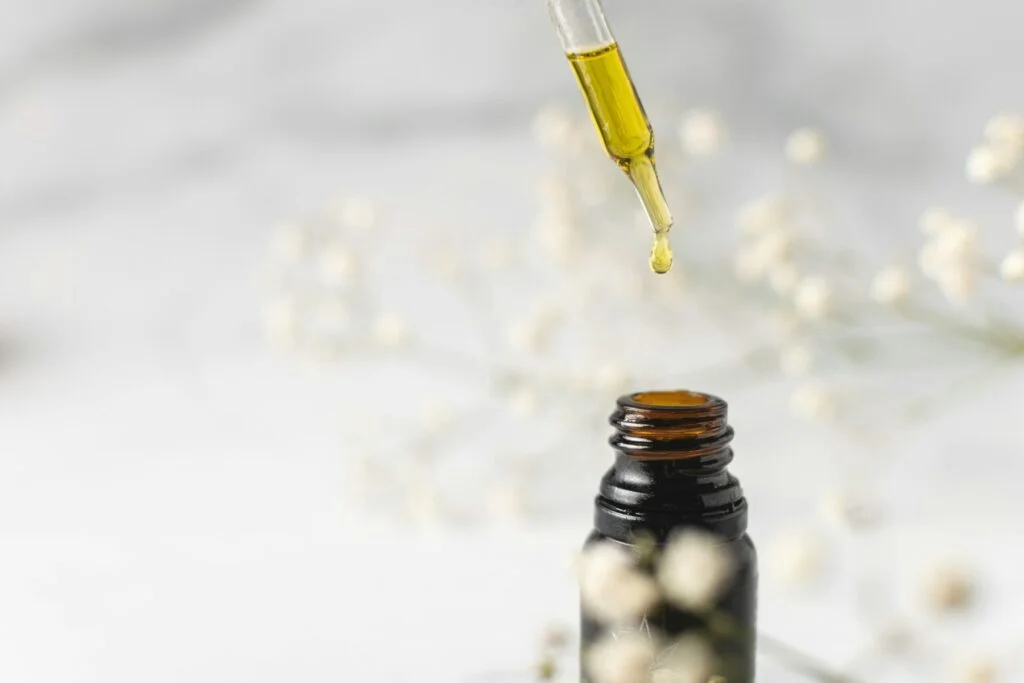 A dropper releasing a drop of golden herbal tincture into a small bottle