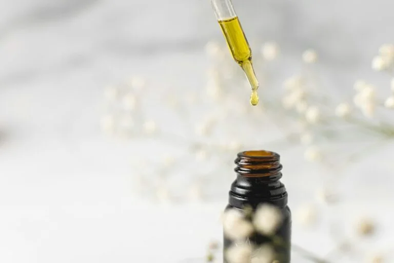 A dropper releasing a drop of golden herbal tincture into a small bottle