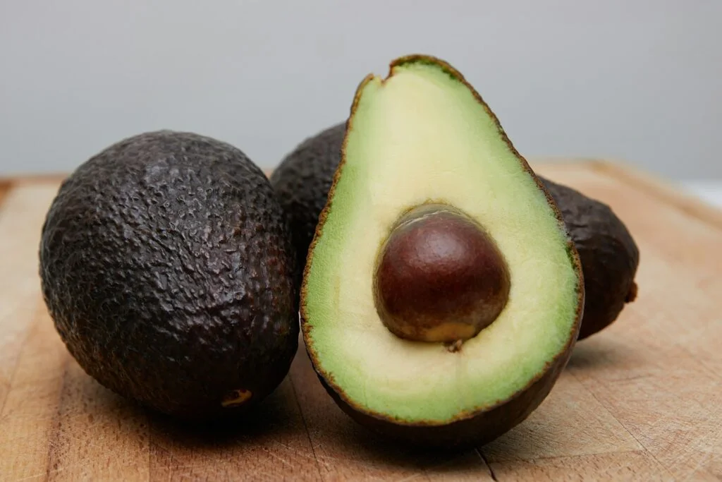 Whole avocados and a halved avocado with its stone on a wooden board