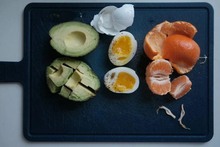 Boiled eggs, avocado and a peeled clementine on a dark chopping board, foods that contain B vitamins