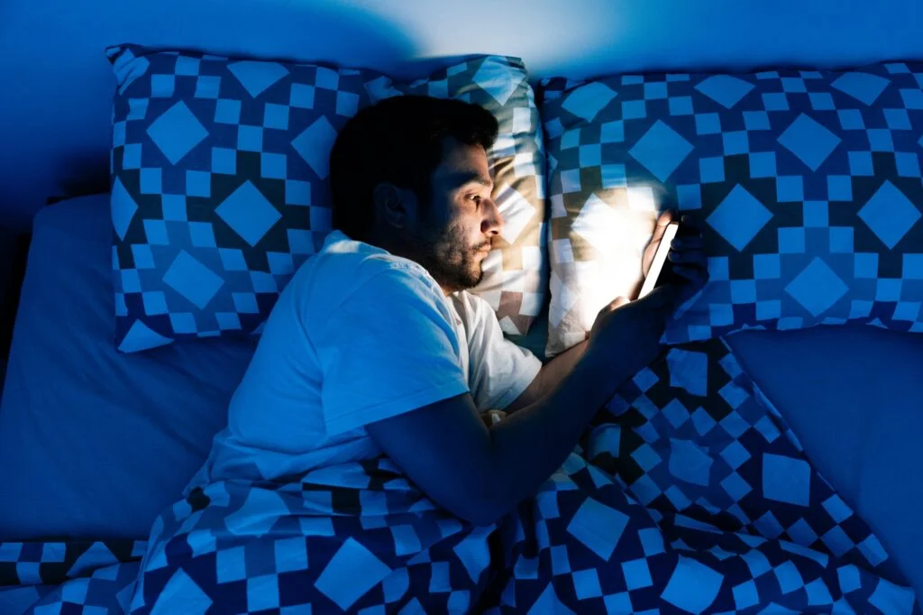 A man in bed at night looking at a bright phone screen