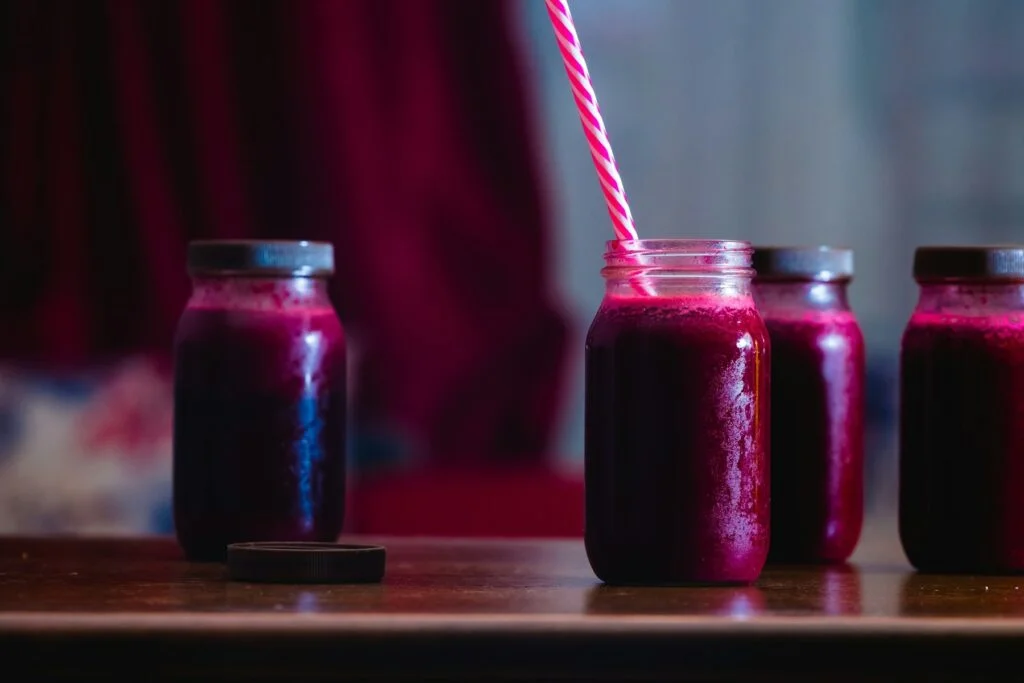Glass jars of deep red beetroot juice, one with a striped straw