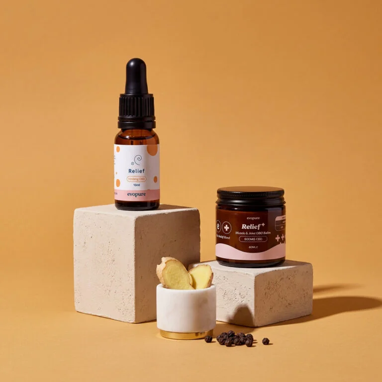 Evopure Relief+ CBD oil with turmeric and Relief+ CBD balm on ochre plinths with fresh ginger