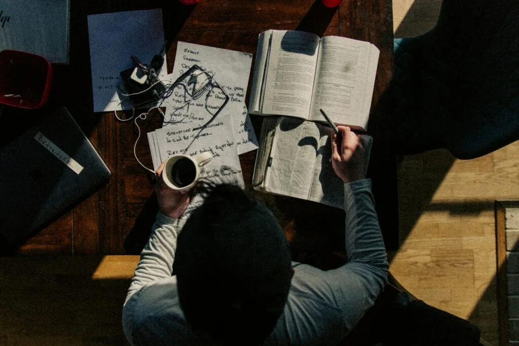 Person working at a desk with notes, a book and a cup of coffee, concentrating on a task