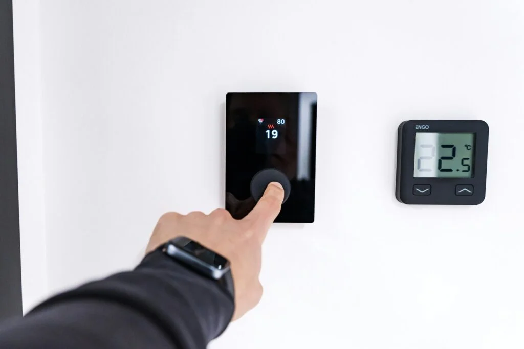 Finger adjusting a digital thermostat on a wall