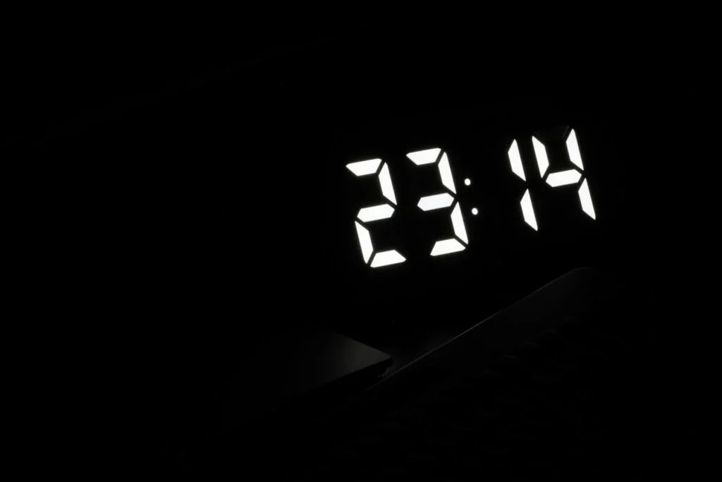 Digital bedside clock glowing 23:14 in a dark room