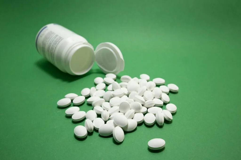 White tablets spilling from a supplement bottle on a green background
