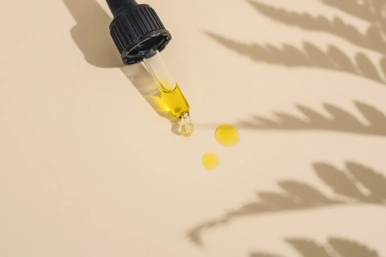 Dropper releasing golden oil beside a leaf shadow