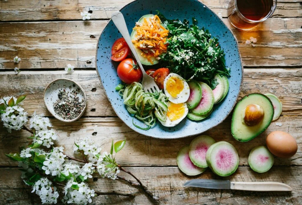 Plate of eggs, greens, avocado, tomatoes and vegetables on a wooden table
