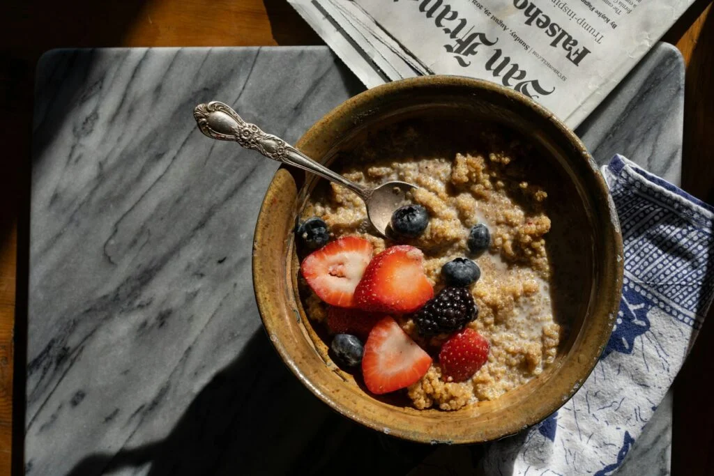 A bowl of porridge topped with strawberries and blueberries on a marble table