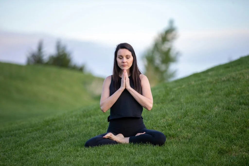 Woman sitting cross-legged on grass with eyes closed, breathing slowly